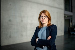 Frau mit blauem Blazer und verschrenkten Armen vor einer Betonwand