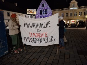 Zwei Menschen mit einem Banner "Mahnwache für die Demokratie Omas gegen Rechts" auf dem Pfaffenhofener Hauptplatz bei Nacht.