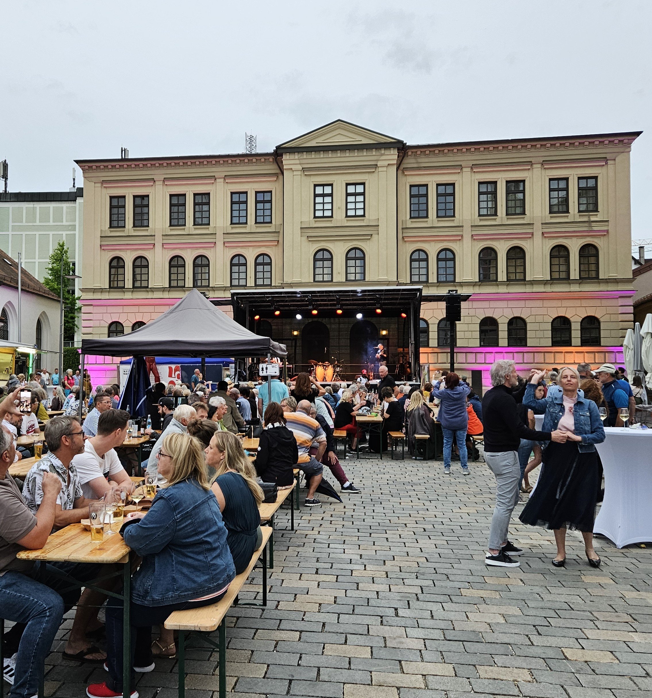 Haus der Begegnung mit Menschen und mit Bühne davor.