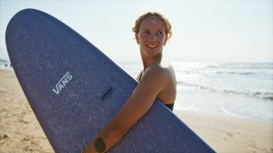 Frau mit Surfbrett in der Hand am Strand.