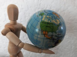 Holzfigur in Menschenform hält einen Globus in den Armen