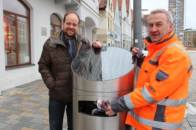 Andreas Herschmann (links), Klimaschutzreferent des Stadtrats, und Stefan Maier von den Stadtwerken an einem der neuen Hightech-Abfalleimer auf dem Hauptplatz.