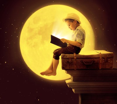 Cute little kid reading a book in the moon light