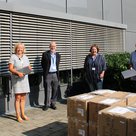 Das Amt für Soziales der Stadt erhält vor dem Gebäude die gespendeten Laptops der Firma Sankyo Daiichi. Diese sind in großen Kartons. Symbolisch dafür halten die Betriebsleiter zwei Laptops in der Hand.