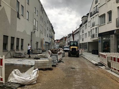 Blick auf die Baustelle in der Auenstraße von der Scheyererstraße. Ein Mann trägt die Pflastersteine für den Weg und ein anderer sitzt in einem Baustelltransportwagen.