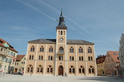Das Rathaus im Pfaffenhofen bei gutem Wetter. Der Platz ist leer. Nur ein Fahrradfahrer und eine Familie befinden sich dort.