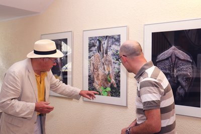 Zwei Männer, einer mit weißem Hut und der andere mit Glatze, begutachten ein Foto von einem Hasen, der Kräuter isst.