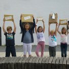Sieben Kinder, ca. zwischen 6 und 8 Jahren, halten Pakete mit den Gewinnen aus dem Lesewettbewerb in die Höhe. 3 Buben und 4 Mädchen sieht man. Alle Kinder lächeln..