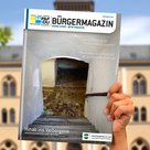 Eine Hand hält das neue Bürgermagazin in die Höhe. Im Hintergrund das Rathaus Pfaffenhofen