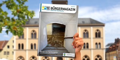 Eine Hand hält das neue Bürgermagazin in die Höhe. Im Hintergrund das Rathaus Pfaffenhofen