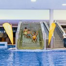 Ein Hallenbad. Auf der Rutsche ein Mann in gelber Badehose und zwei Kinder