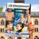Hand hält das aktuelle Bürgermagazin in die Höhe. Im Hintergrund ist das Pfaffenhofener Rathaus zu sehen.