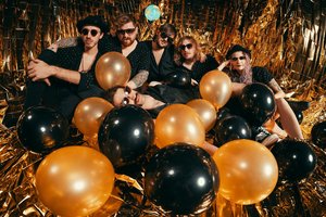 Band umringt von Luftballonen und Glitzergirlanden.