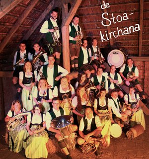 Gruppenfoto der Musikkapelle mit ihren Instrumenten in einem alten Stall.