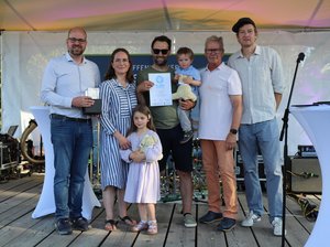 Familie mit zwei Kindern steht mit Urkunde und Pokal auf der Bühne