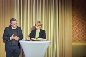 Bürgermeister Thomas Herker und Paula van Well im Festsaal; Paula van Well trägt sich in das goldene Buch an einem Stehtisch ein.