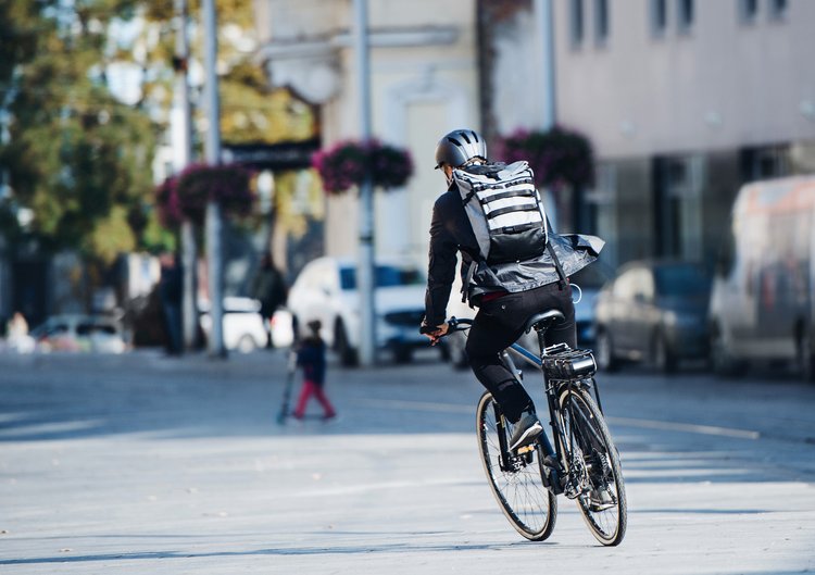 Fahrradfahrer mit Rucksack und Helm auf einer Straße.