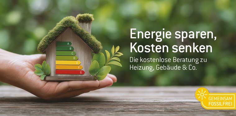 Hand die ein Haus in der Hand hält mit einer Energieskala drauf. Im Hintergrund grüne Blätter