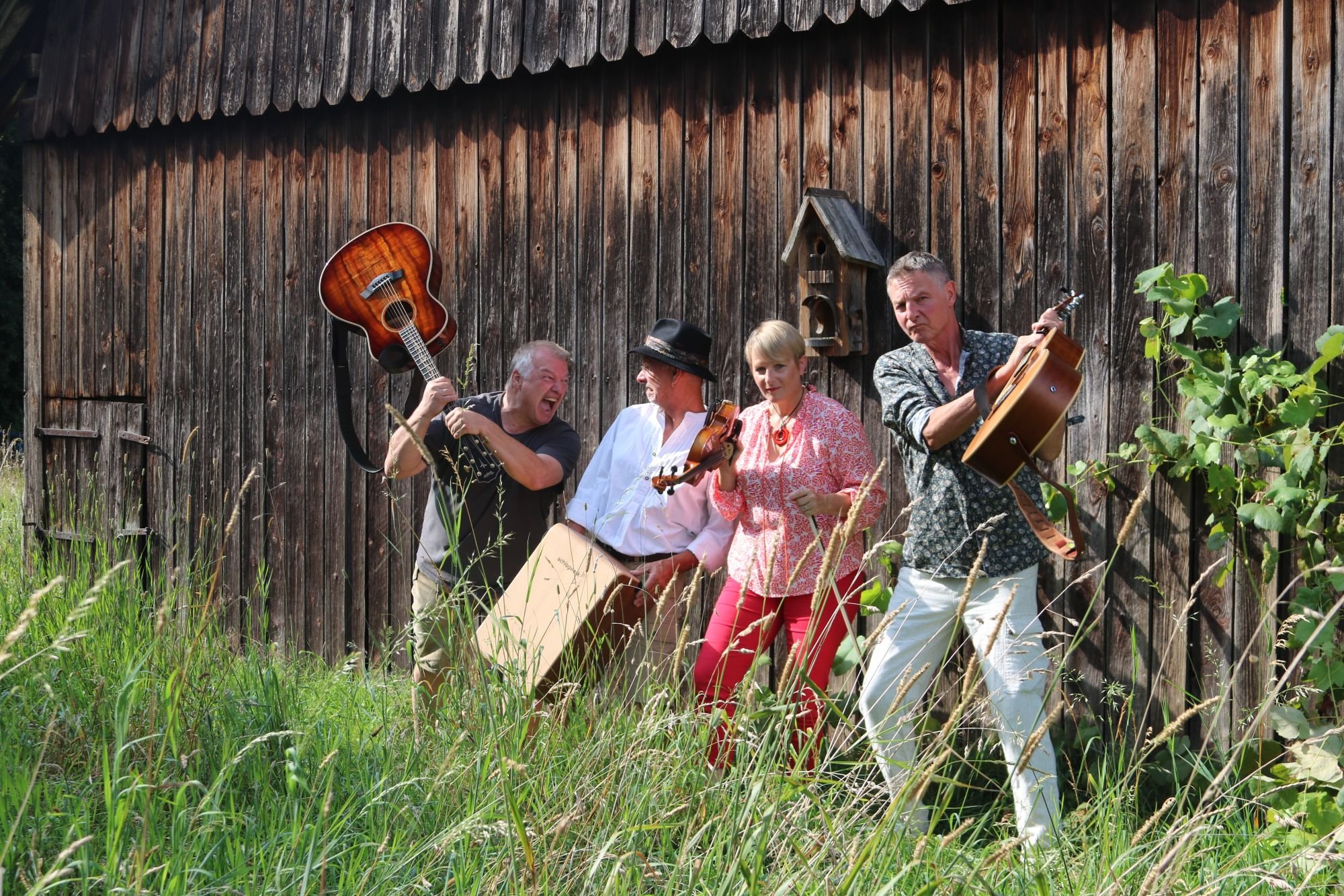 Band auf einer Wiese vor Holzfassade mit Instrumenten
