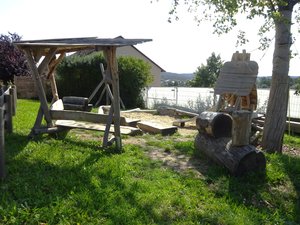 Spielplatz mit Holz-Spielgeräten, Sandkasten, grüner Wiese und einer Bank