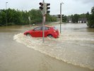 rotes Auto auf überschwemmter Straße, Wasser steht bis zur halben Höhe der Räder
