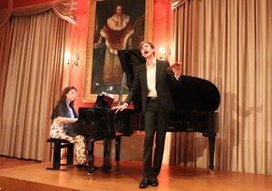 Daniel Sauer singend auf der Bühne im Rathaus Festsaal neben dem Klavier.
