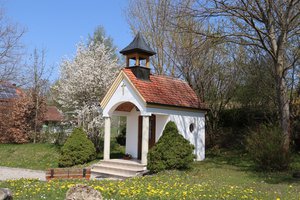 Kapelle bei Uttenhofen mit einer Bank und blühender Wiese davor. Dahinter ein blühender Kirschbaum