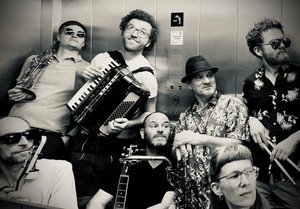 Foto der Band in einem Aufzug mit Instrumenten, schwarz-weiß.