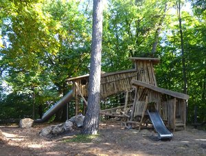 Spieplatz mit großem Kletterturm aus Holz und Bäumen außen herum