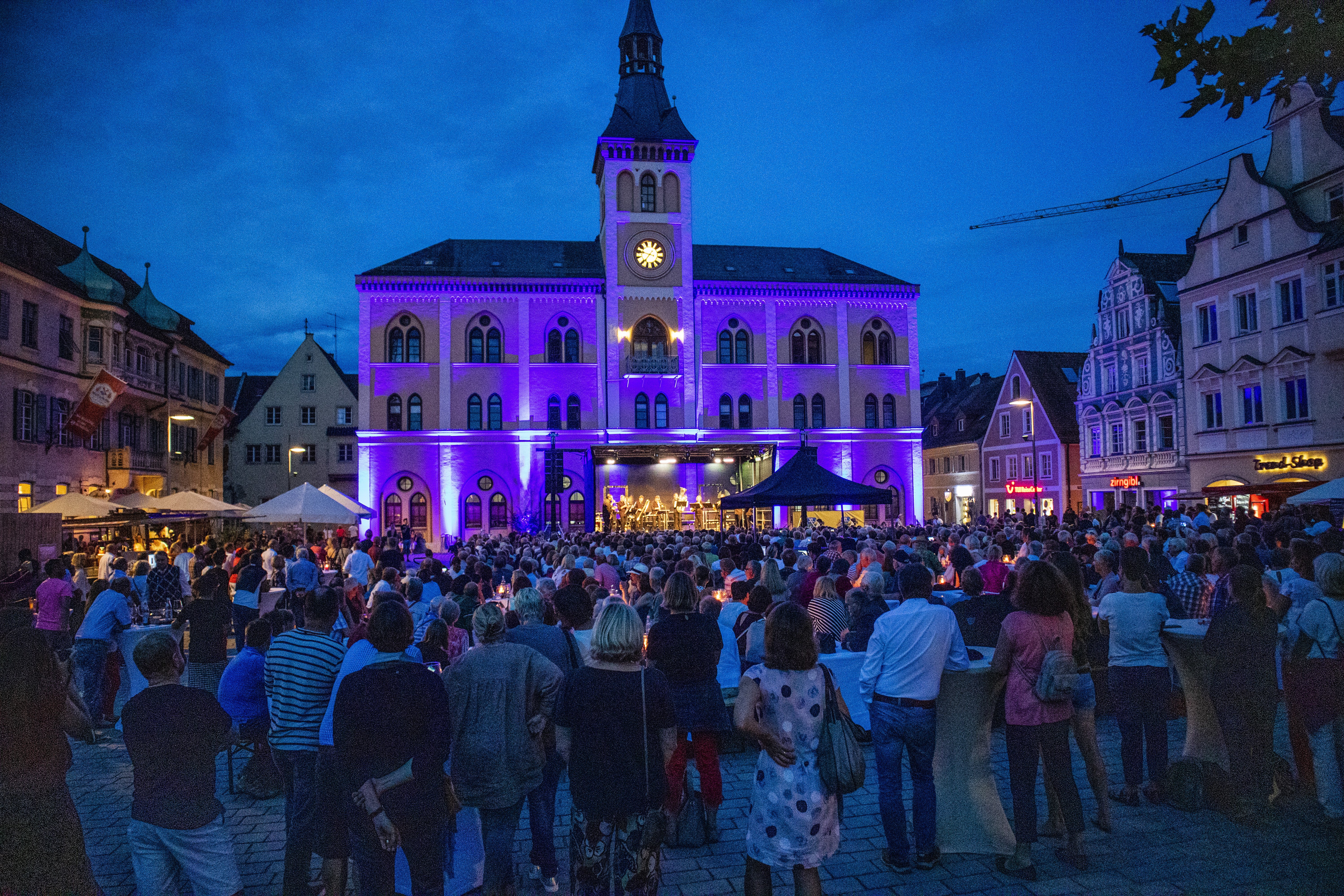 Rathaus bei Dämmerung in blau/lila Farben bestrahlt, zahlreiche Menschen vor einer Bühne