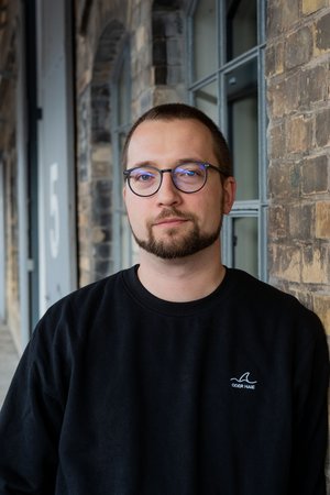 Portrait-Aufnahme vom Lutz-Stipendiat Peter Thiers vor einem Backsteingebäude