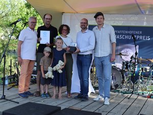 Familie mit zwei Kindern steht mit Urkunde und Pokal auf der Bühne