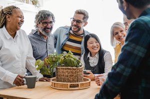 Verschiedene Menschen stehem im Kreis um einen Tisch und unterhalten sich