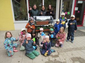 Drei Erwachsene des Elternbeirates stehen gemeinsam mit Kindern rund um den fertig bepflanzten Pflanzwagen und freuen sich.