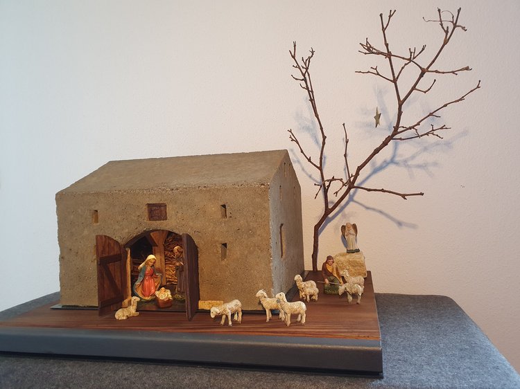 Krippe mit einem Haus, einem kahlen Baum und verschiedenen Figuren wie Menschen und Schafen.
