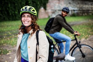 Lachende Frau mit Fahrradhelm im Vordergrund, Mann auf Rad unscharf im Hintergrund
