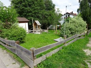 Spielplatz mit hohem Gras, Kletterturm und vielen Büschen außen herum