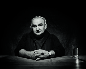 Schwarz-Weiss-Foto von Sigi Zimmerschmied, der an einem Tisch sitzt und in die Hände ineinander gelegt hat.