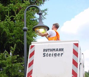 Mensch auf einem Kran wechselt die Leuchte einer Straßenlaterne.
