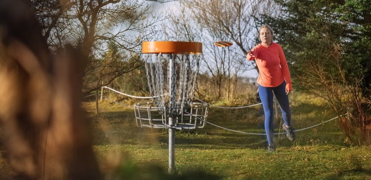 Frau wirft Disc-Scheibe in einem DiscGolf-Parcours